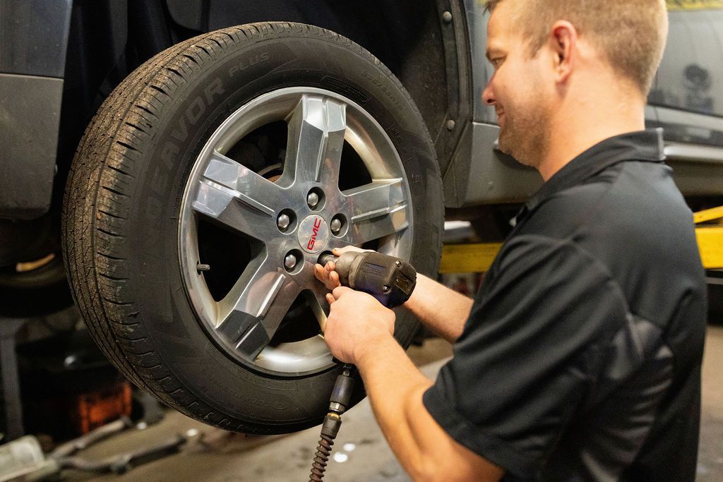 Mechanic using a power tool to remove a car tire in a garage.