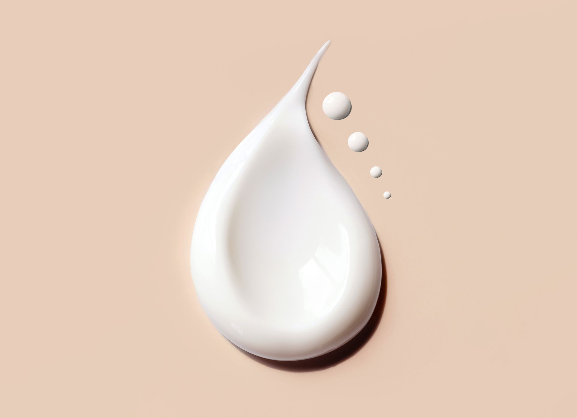Ein Tropfen weißer Flüssigkeit auf beigem Hintergrund.