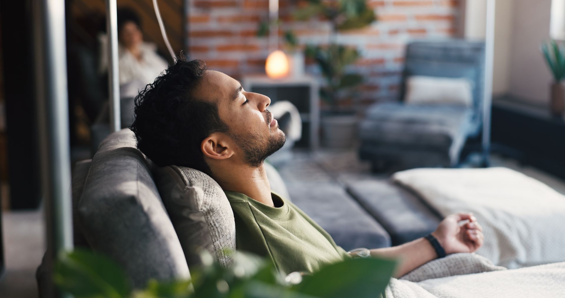 Woman in a white robe receives an IV drip while holding a drink in a bright setting.