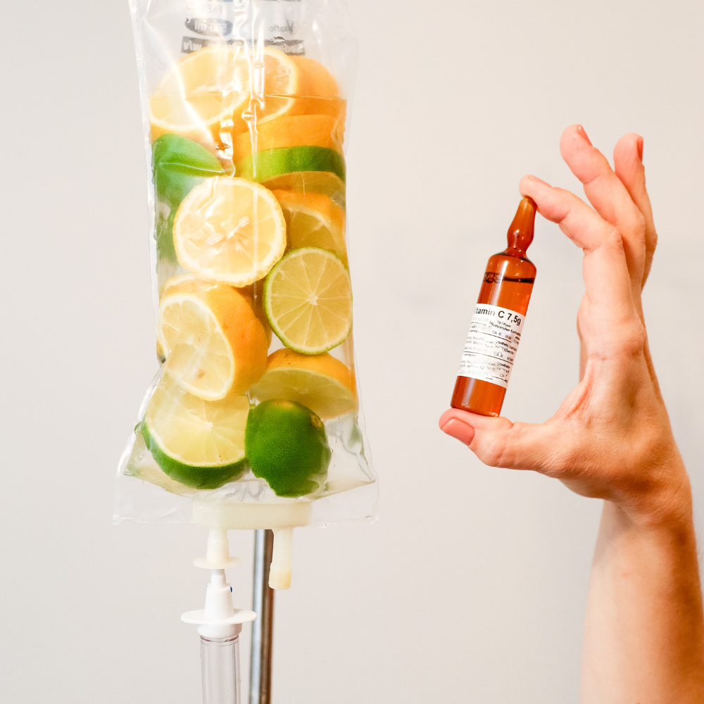 IV bag filled with citrus fruit; hand holds a vitamin C vial.