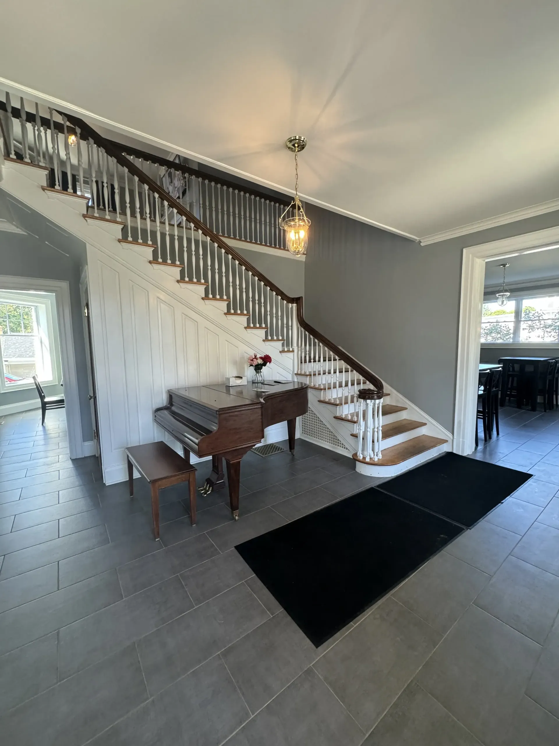 An entryway featuring a grand staircase, a brown piano, gray tile flooring