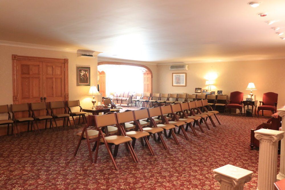 Rows of empty folding chairs arranged for an event in a carpeted room with light-colored walls and wood-paneled doors.
