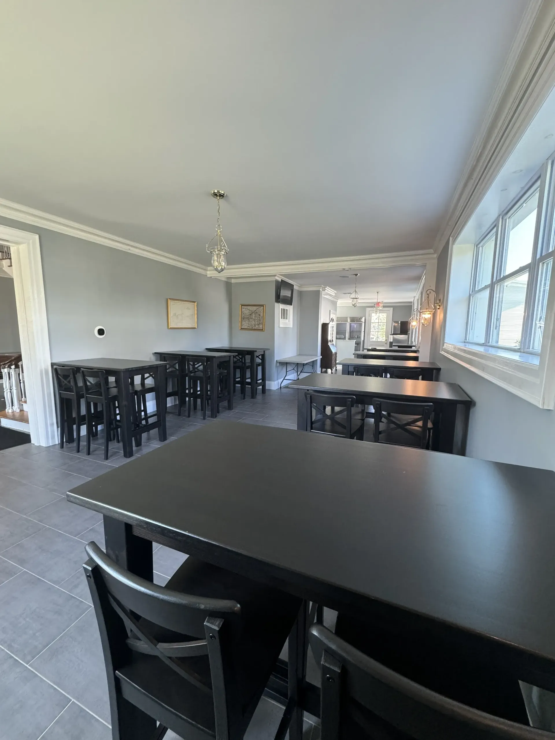 An interior view of a dining room featuring rows of dark wooden tables and chairs set against light grey walls.