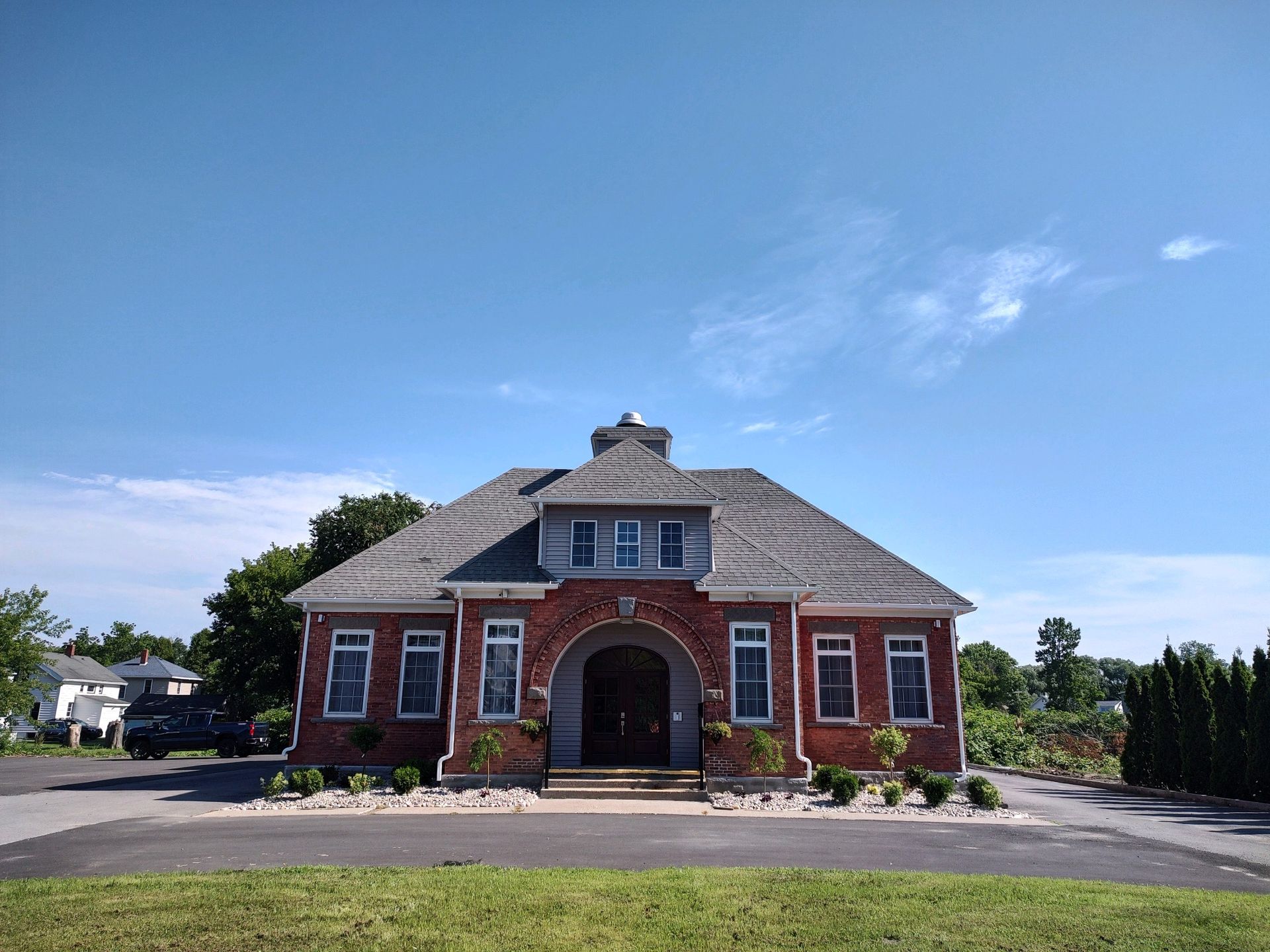 A red brick building with an arched entrance and gray shingled roof under a clear blue sky.