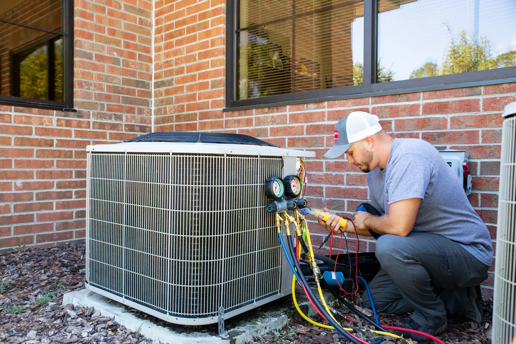 A technician is servicing an air conditioning unit outside a brick building.