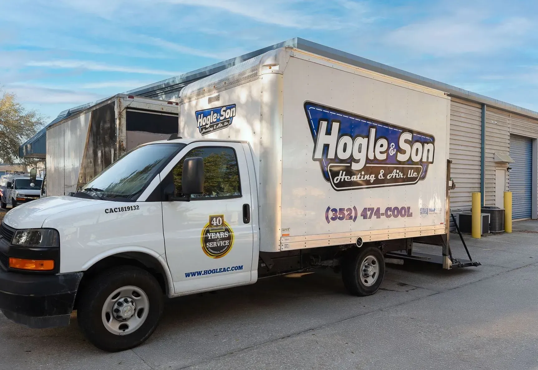 White Hogl & Son box truck parked outside a commercial building on a sunny day.