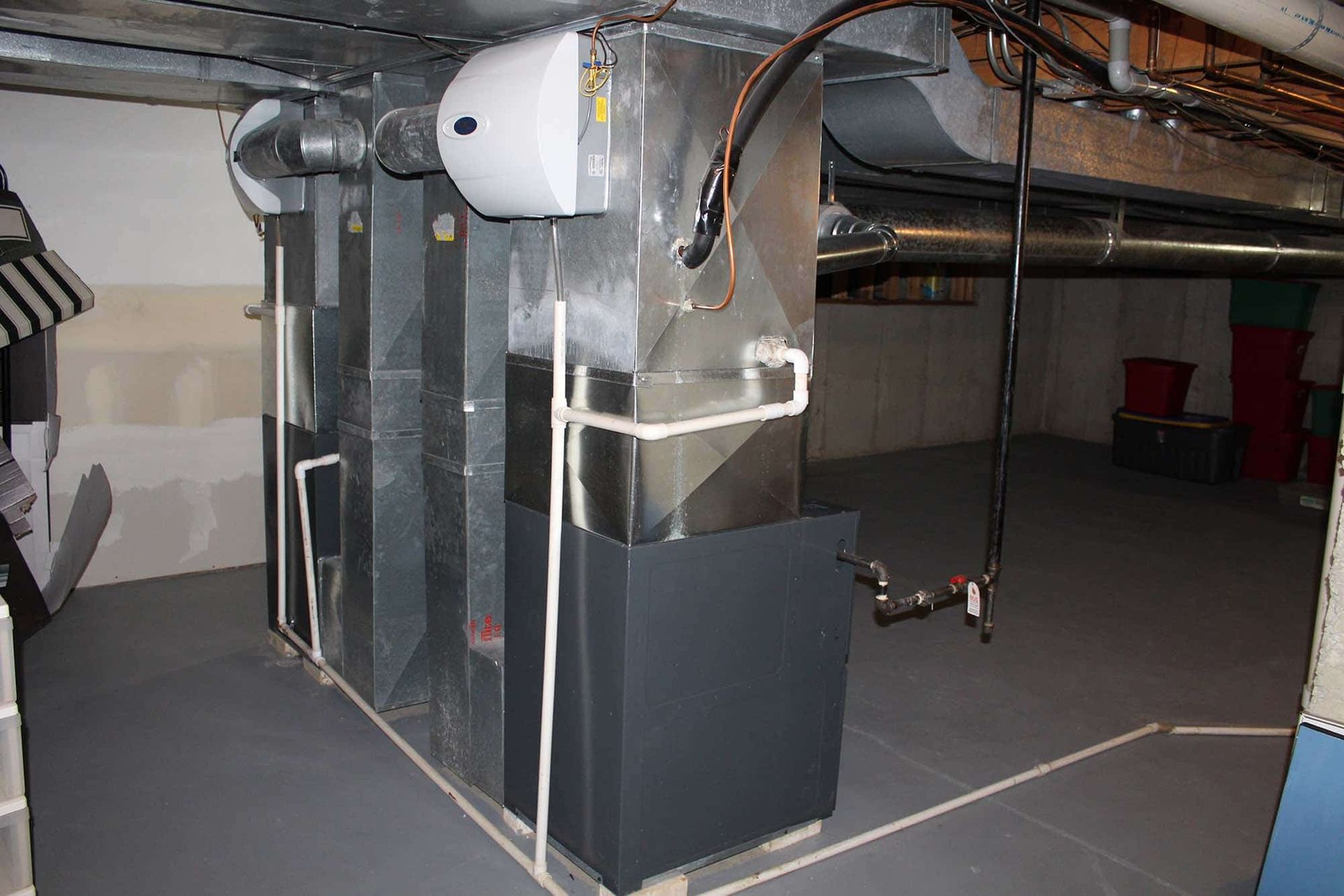 HVAC system in a basement; silver ductwork, humidifier, and a dark grey unit on the floor.