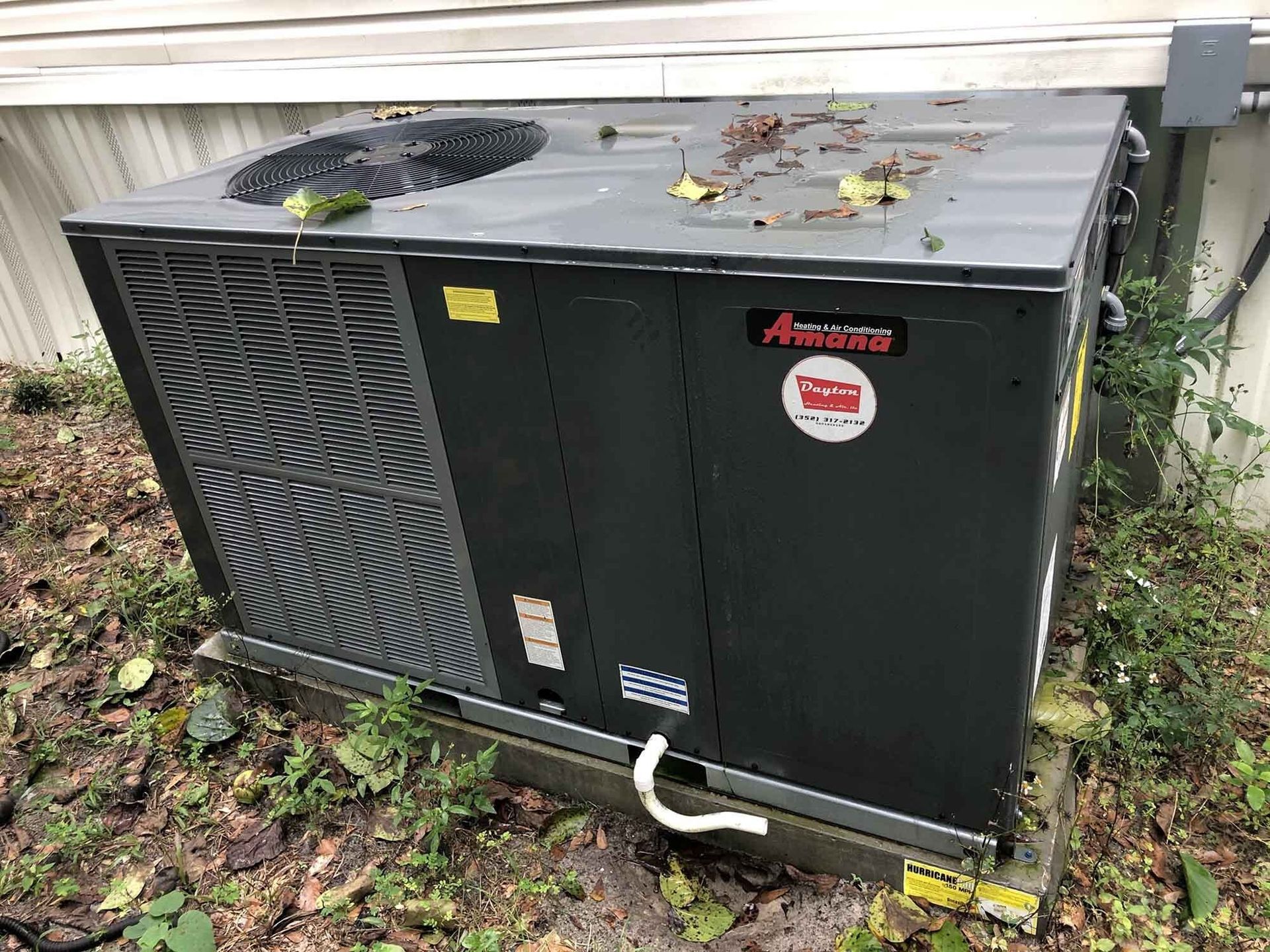 Outdoor air conditioning unit; black with fan and coil; debris on top.