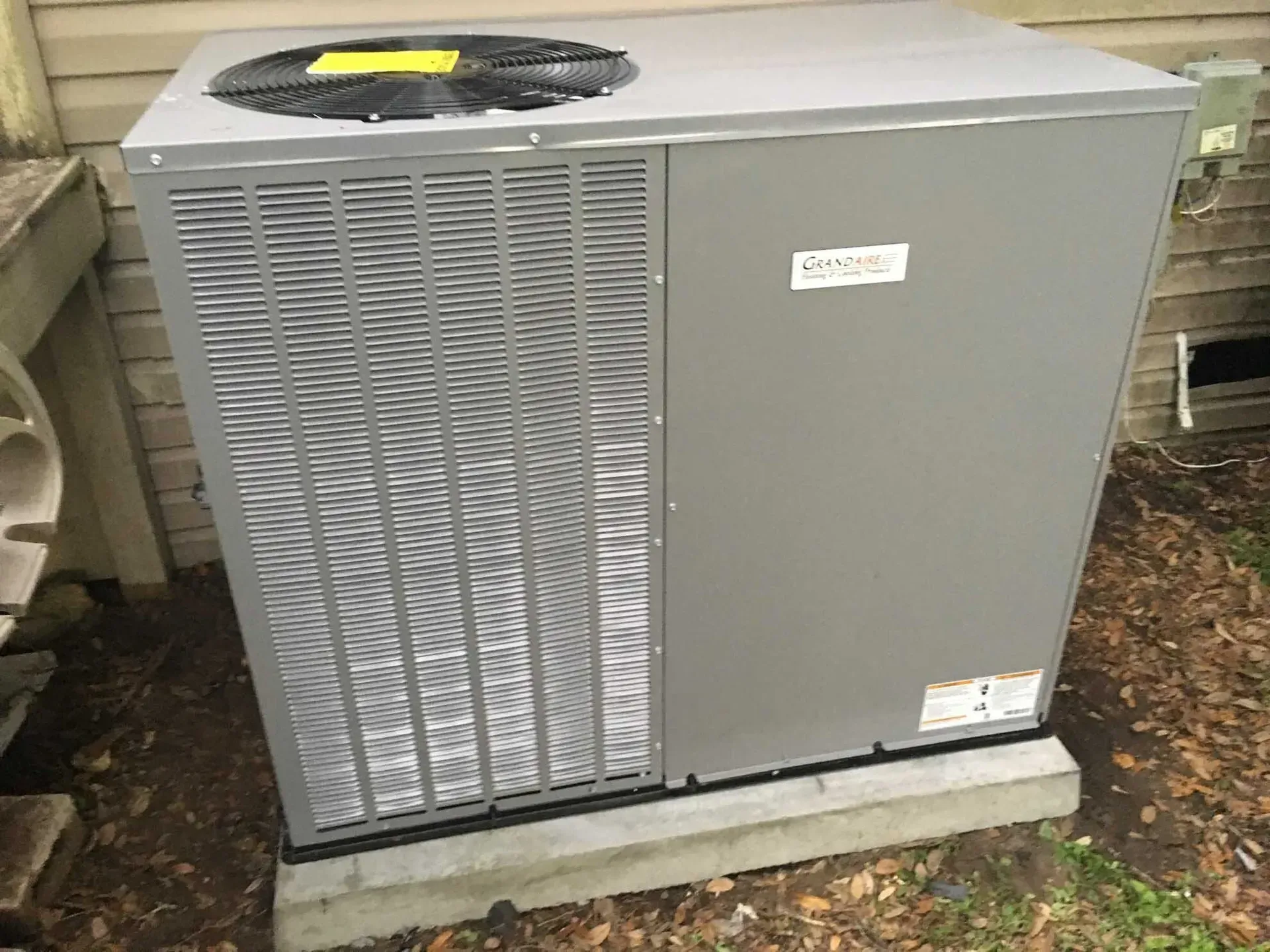 Gray air conditioning unit on concrete base next to a house.