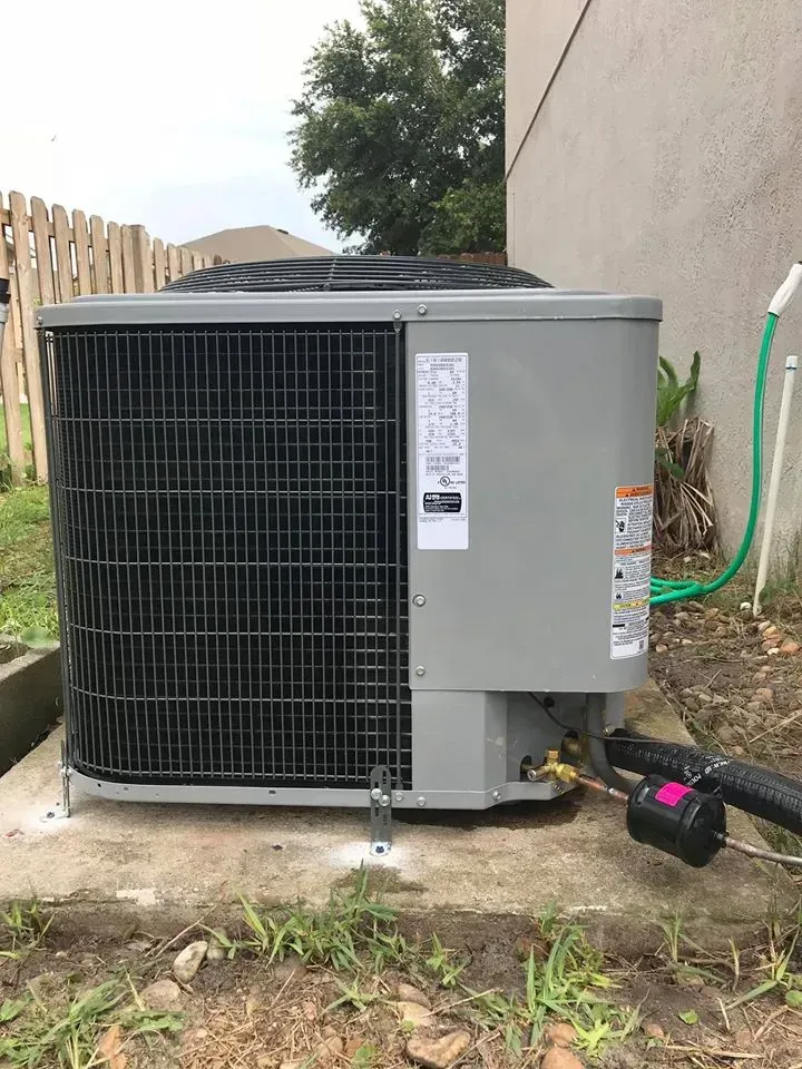 Air conditioning unit outside a building, gray and black with a green hose nearby.