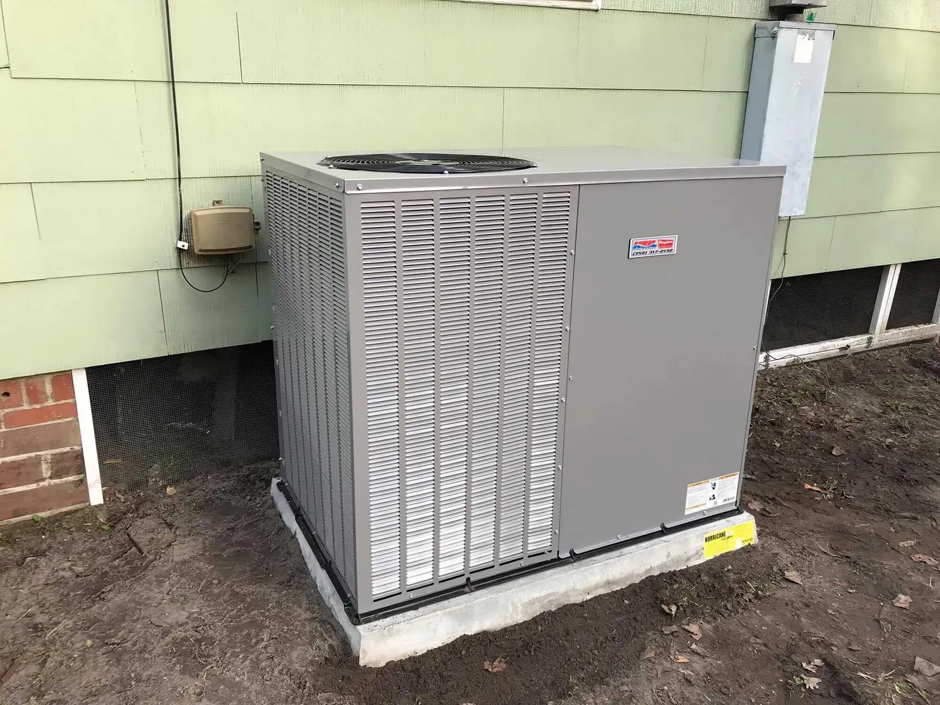 Gray HVAC unit next to a light green house wall, on a concrete pad.