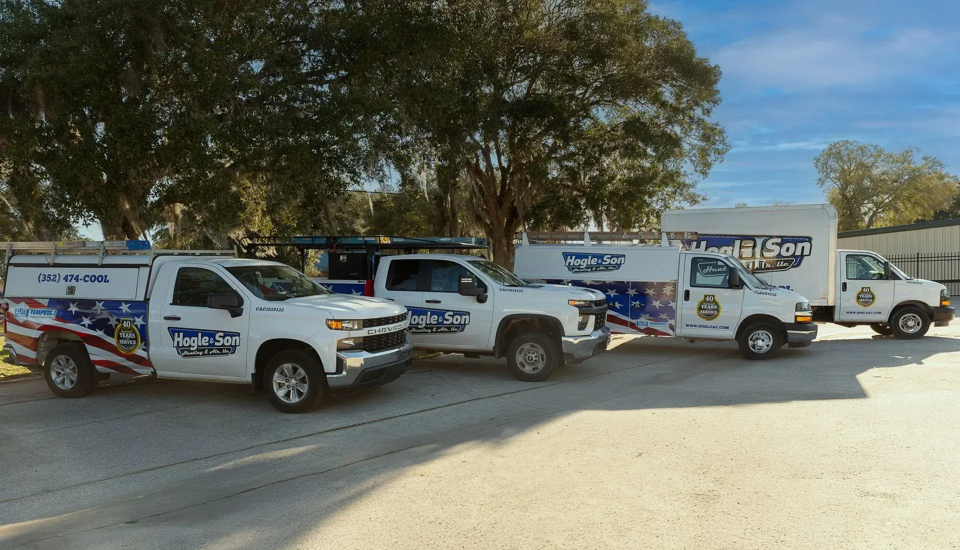 Four white service trucks with American flag graphics parked outside on a sunny day.