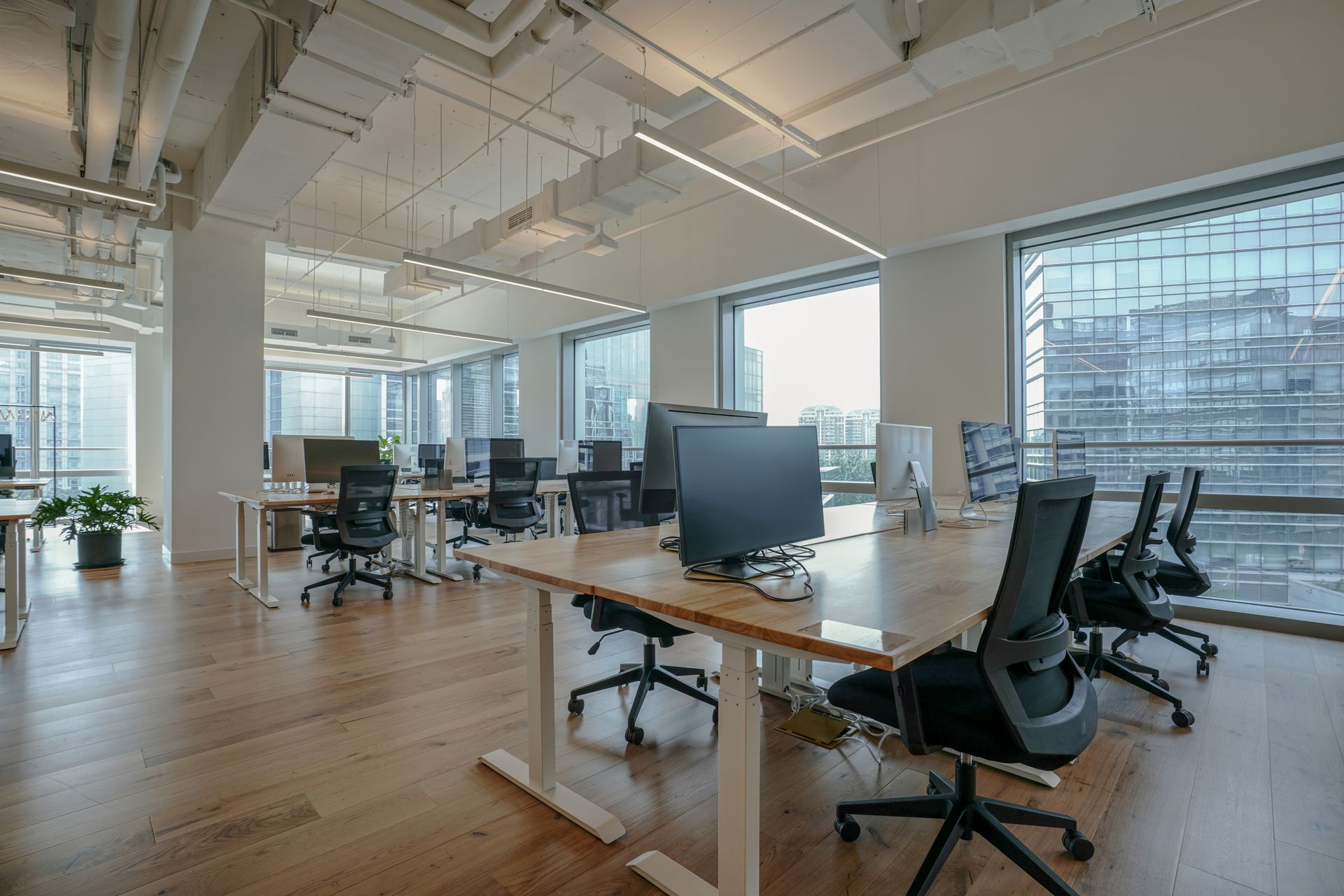 Open-plan office with desks, computers, and chairs. Large windows offer a city view, wooden floors.