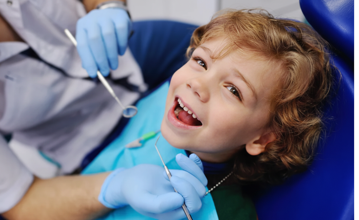 Ragazzo sulla poltrona del dentista con la bocca aperta e sorridente. Dentista con guanti e strumenti visibili.