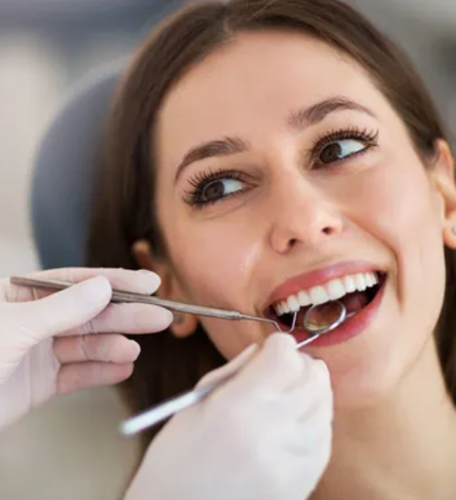 Donna che sorride al dentista durante una visita con strumenti odontoiatrici.