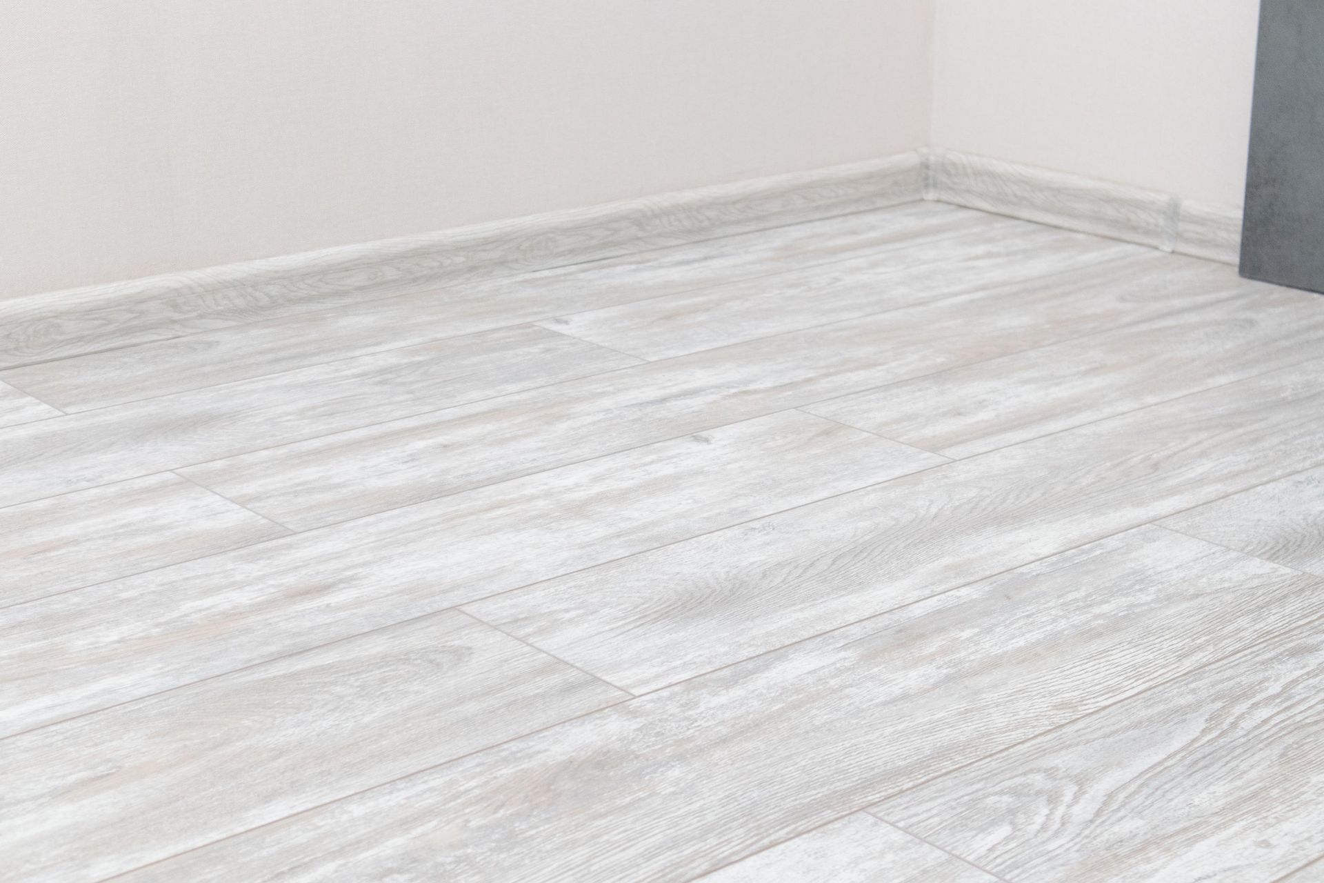 Whitewashed wood-look floor and molding meet light gray walls in a corner.