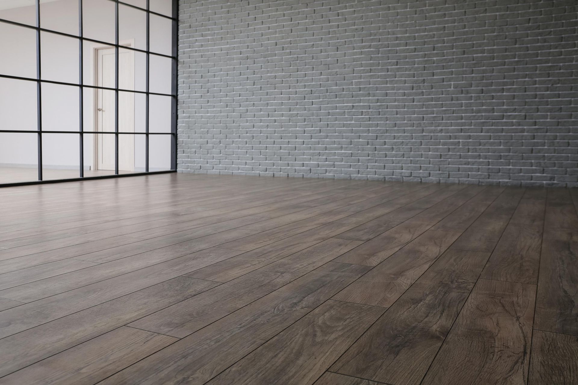 Dark wood floor and gray brick wall in an empty room with a large window.