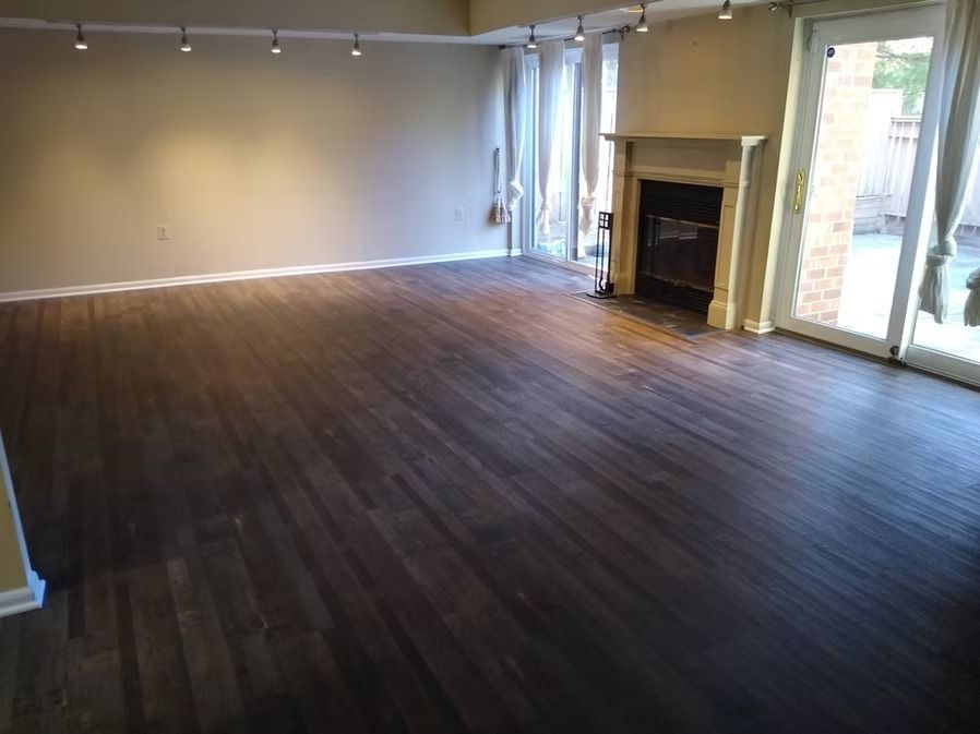 Empty living room with dark wood floors, fireplace, and glass doors leading to a patio.
