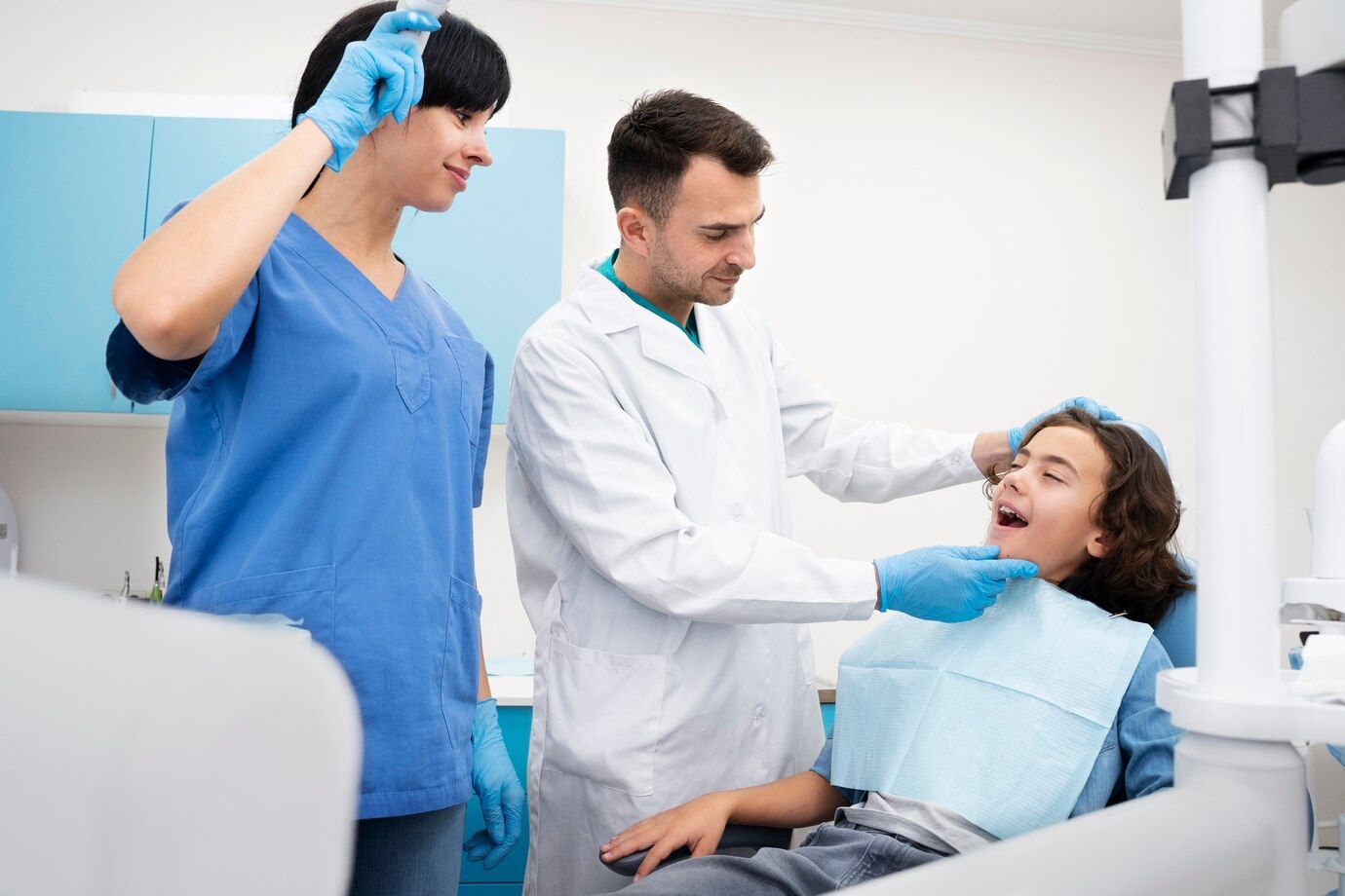 A dentist and a nurse are examining a young boy 's teeth in a dental office.