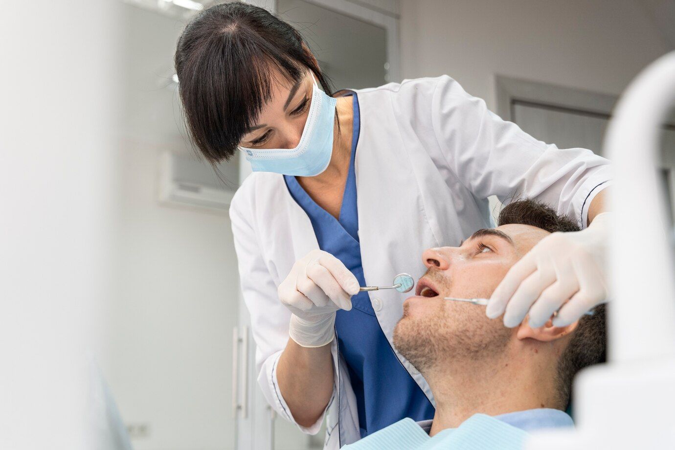A female dentist is examining a man 's teeth in a dental office.