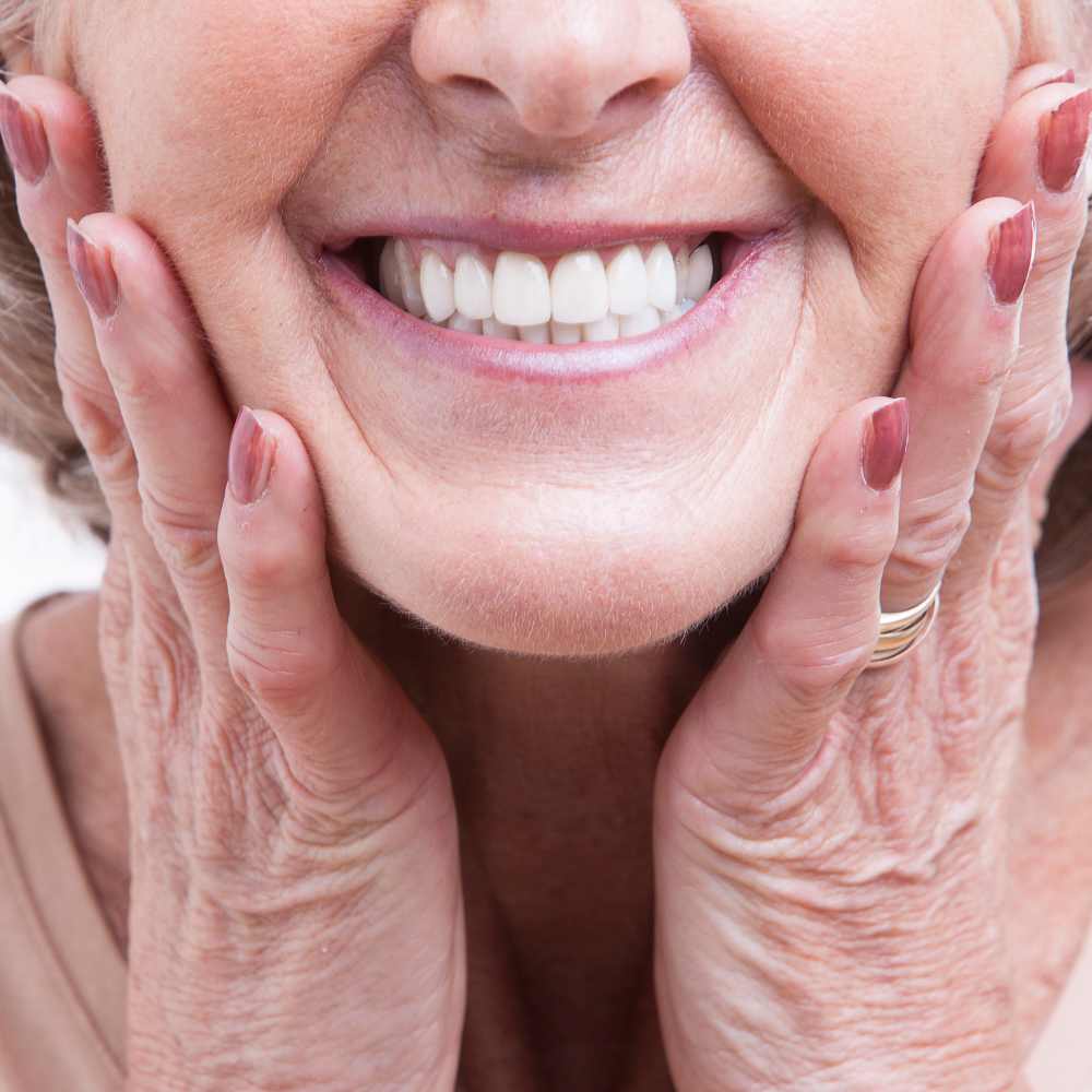 An older woman is smiling with her hands on her face.