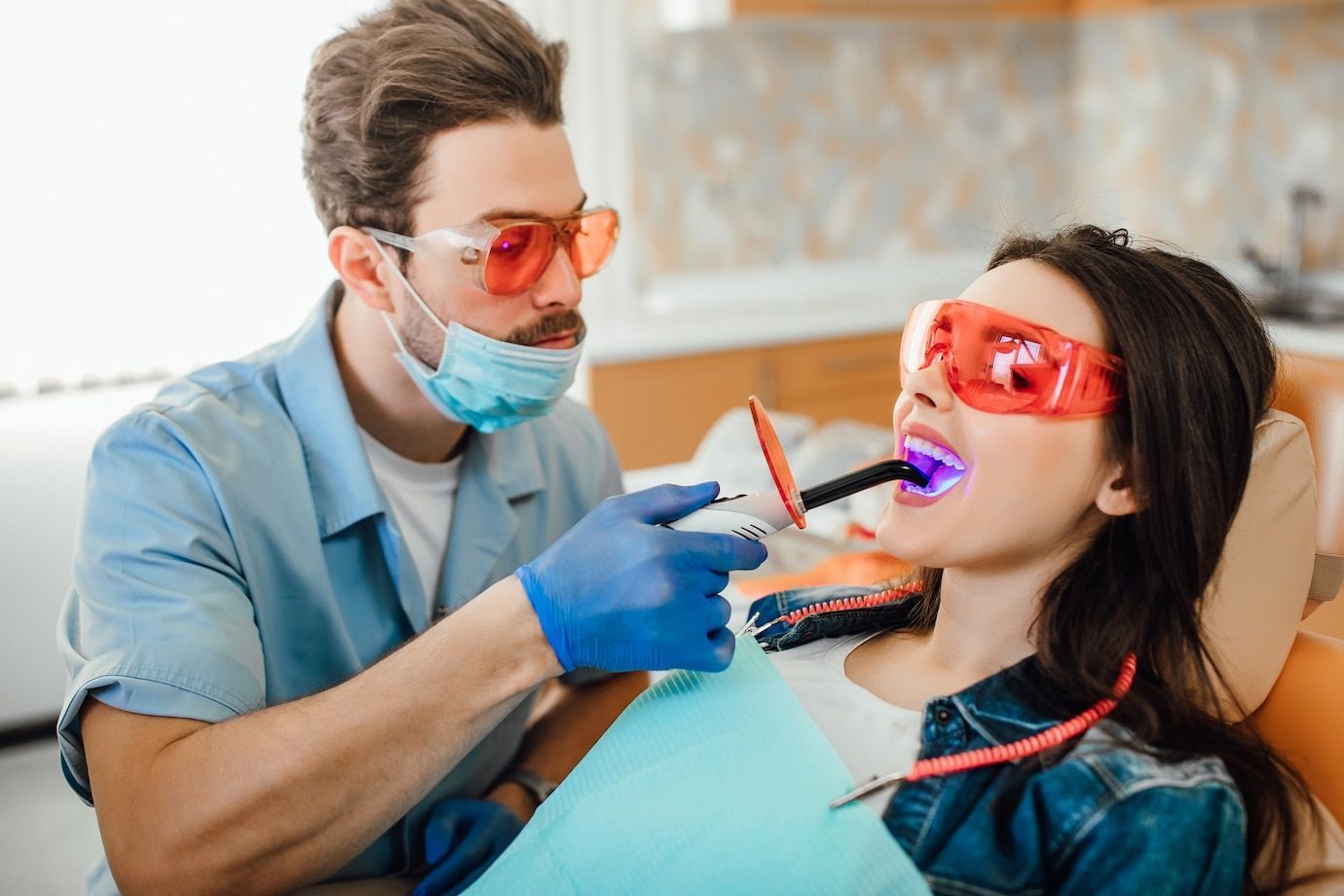 A dentist is whitening a woman 's teeth in a dental office.