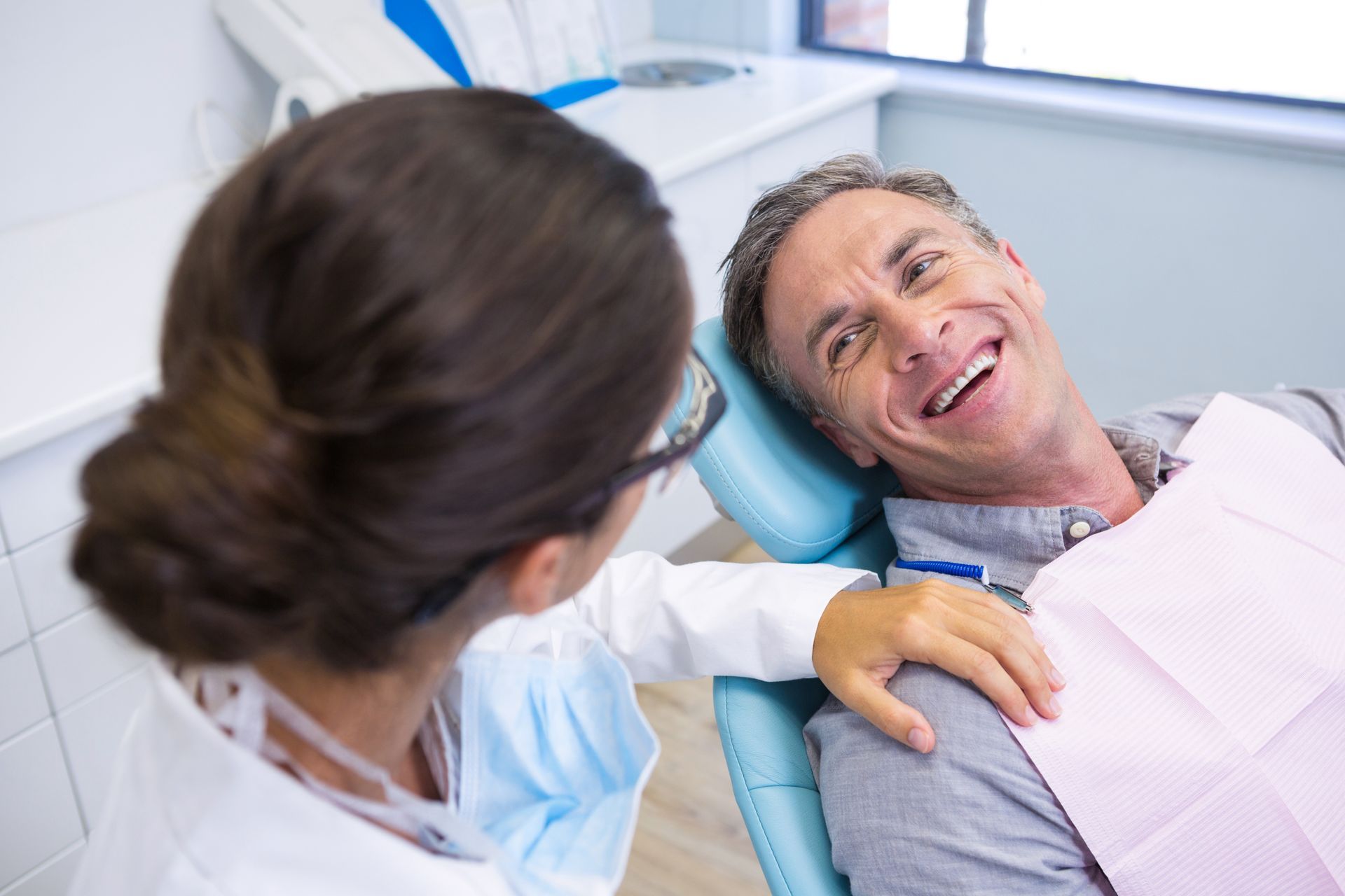 A man is sitting in a dental chair talking to a female dentist.