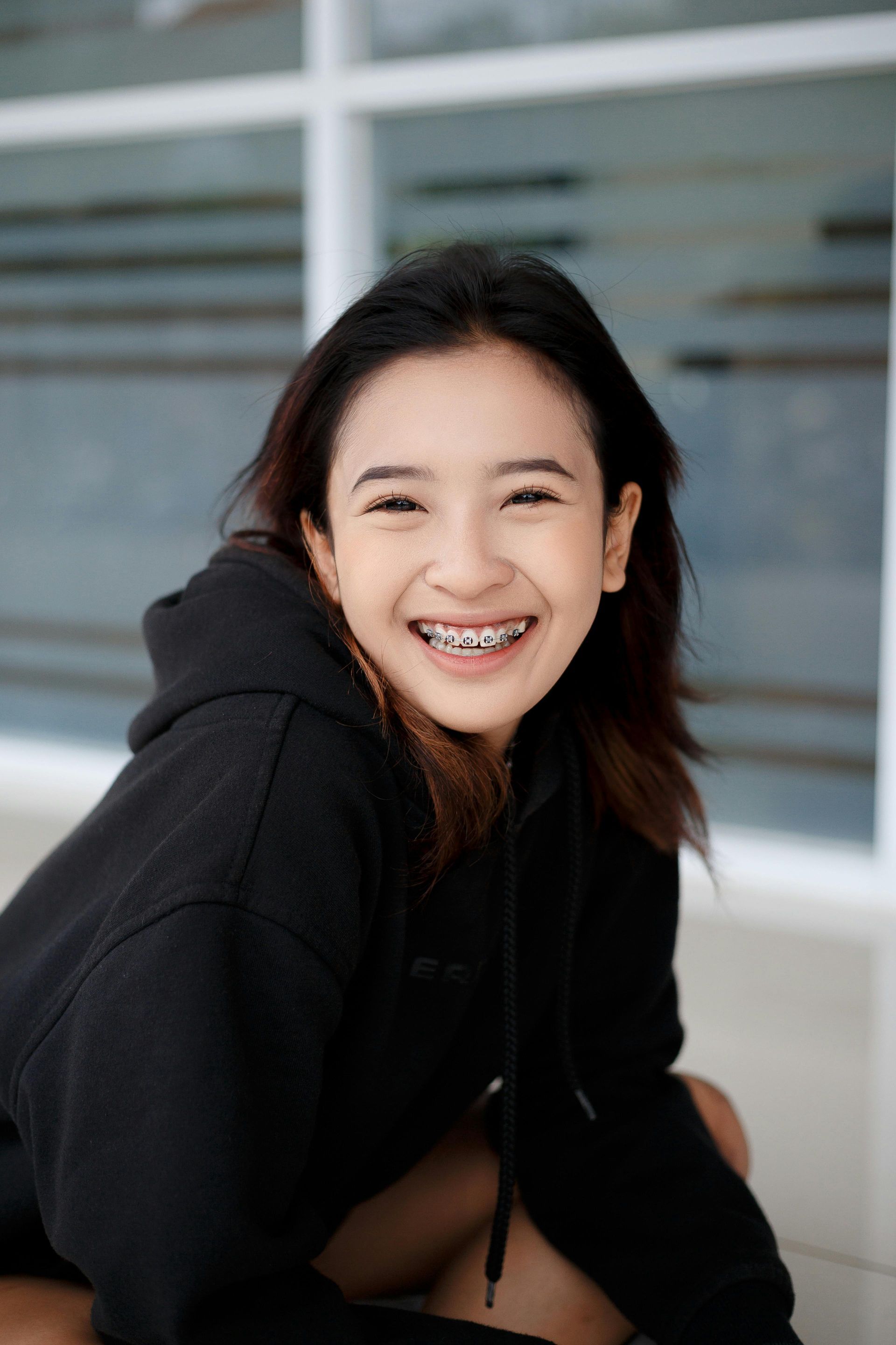 A young woman with braces is wearing a black hoodie and smiling.