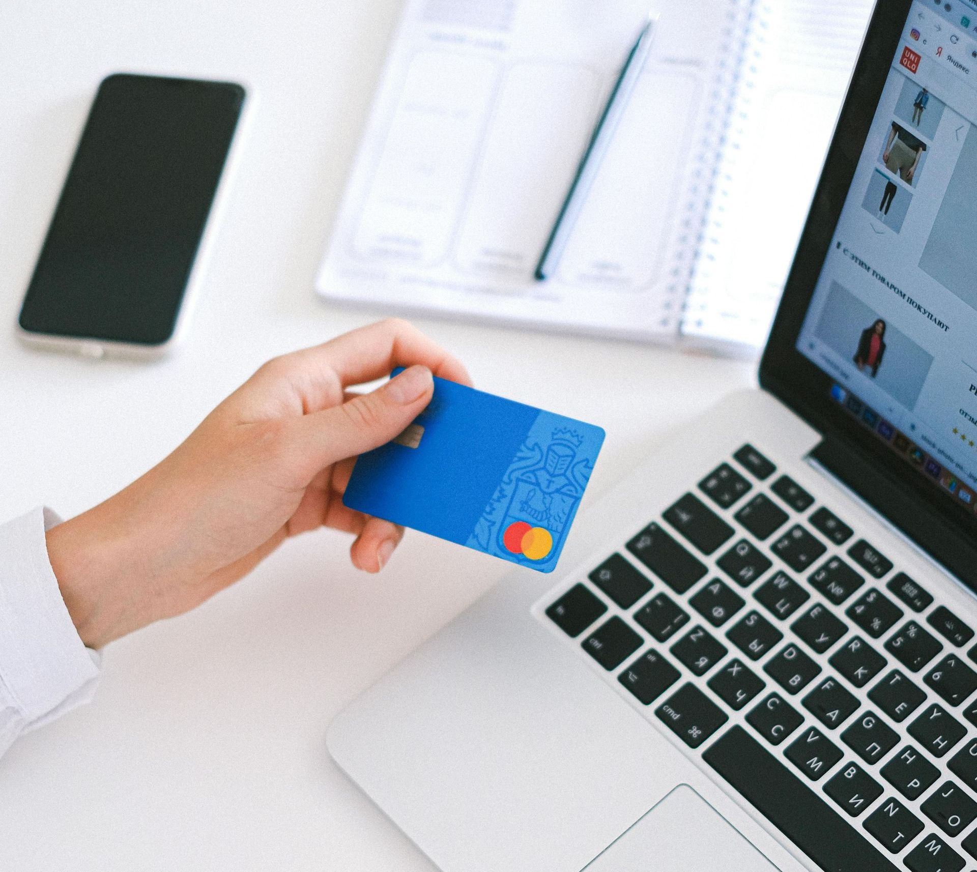 A person is holding a credit card in front of a laptop