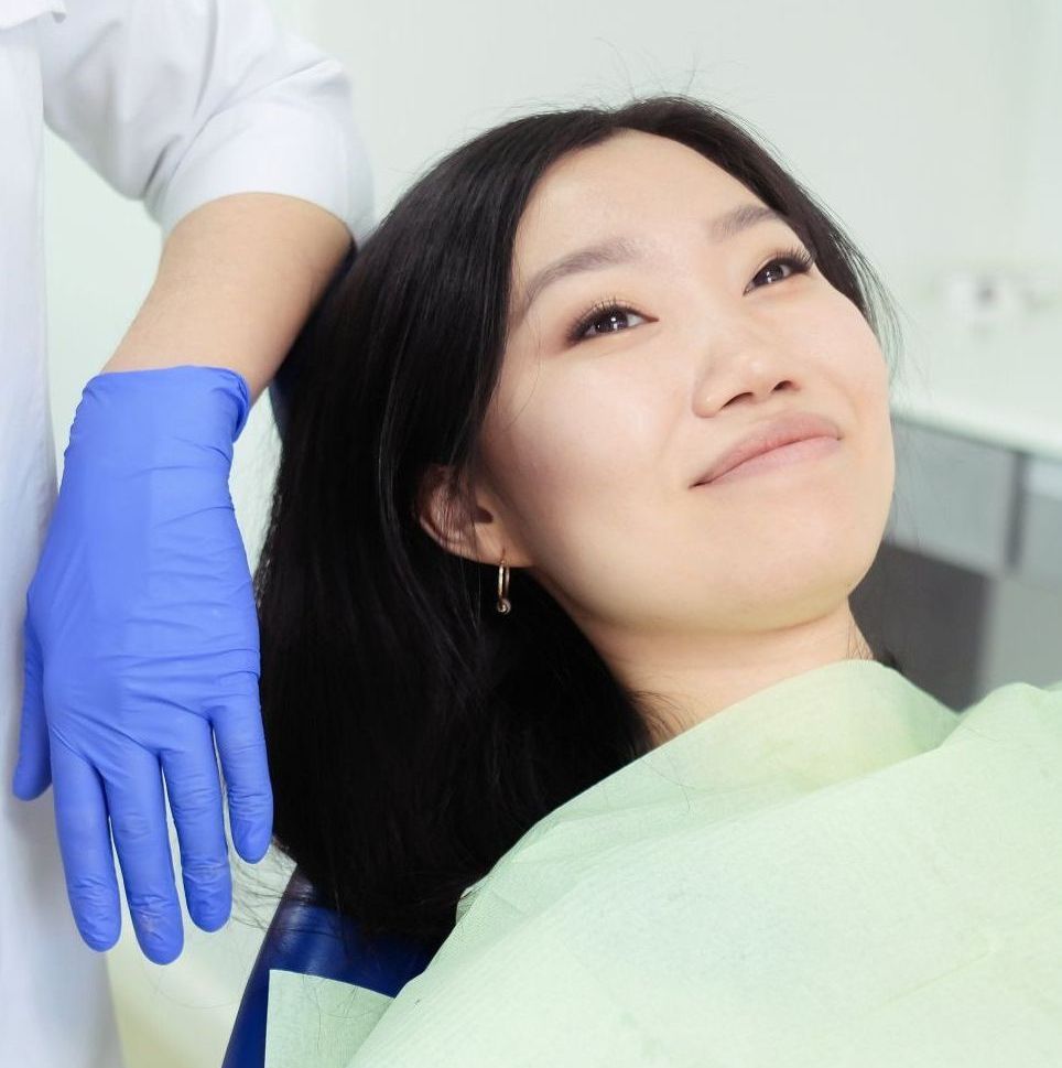 A woman is sitting in a dental chair with a dentist wearing blue gloves