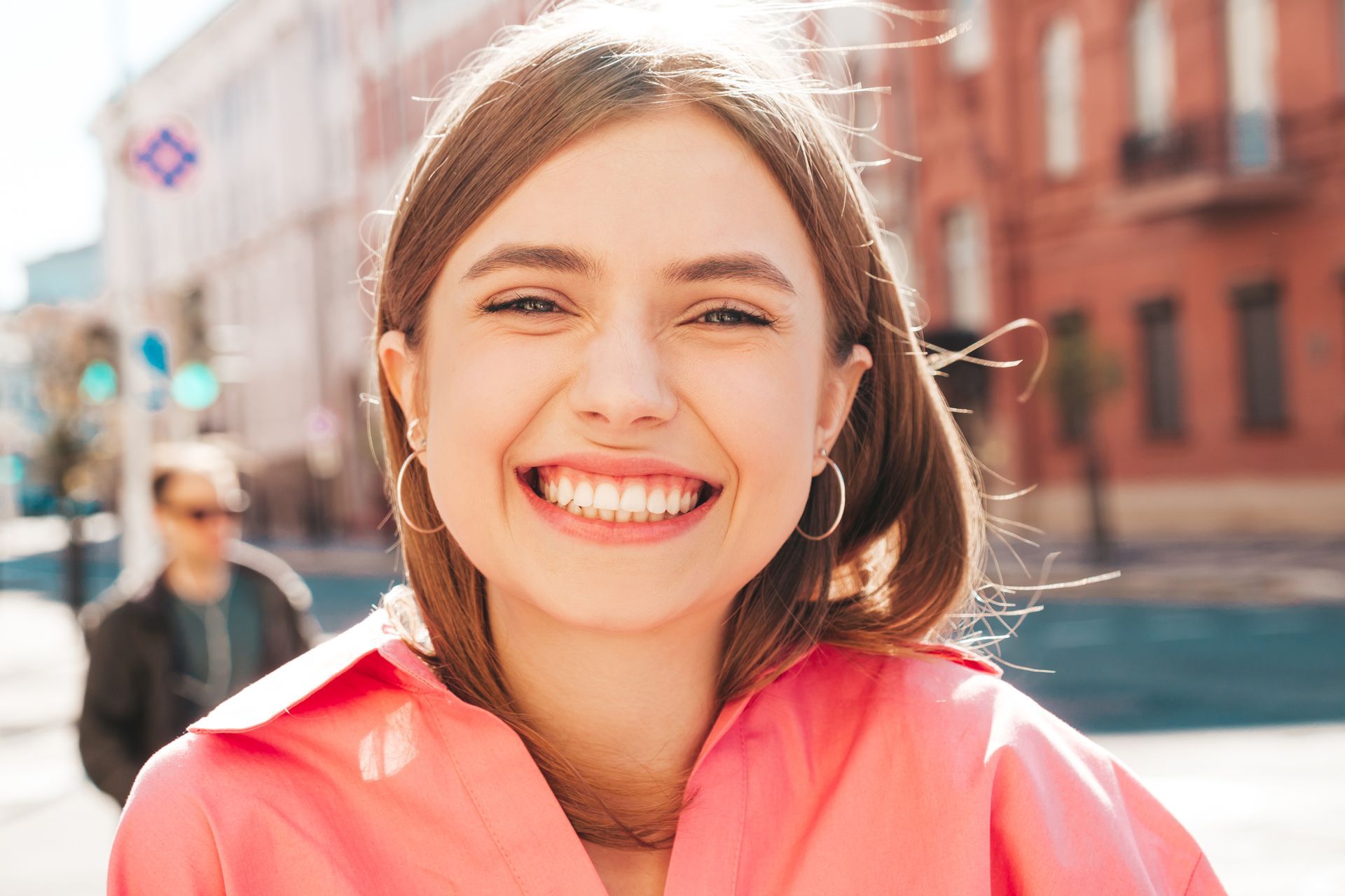 A woman in a pink shirt is smiling and looking at the camera.