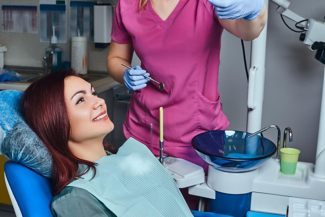 A woman is sitting in a dental chair while a dentist examines her teeth.