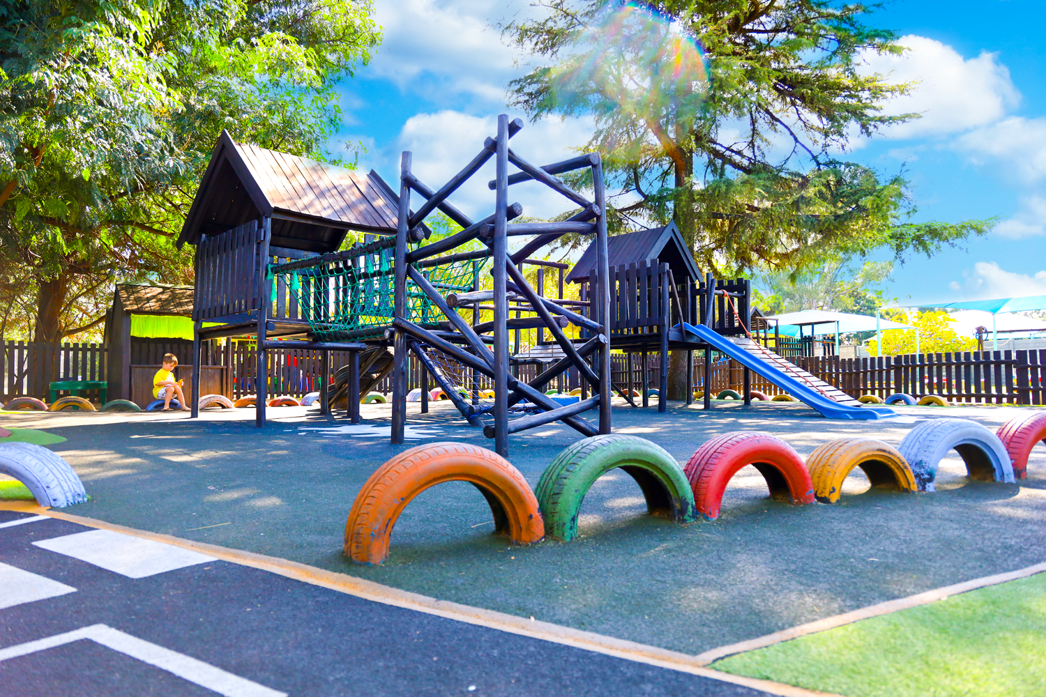 A playground with a slide , stairs , and swings in a grassy field.