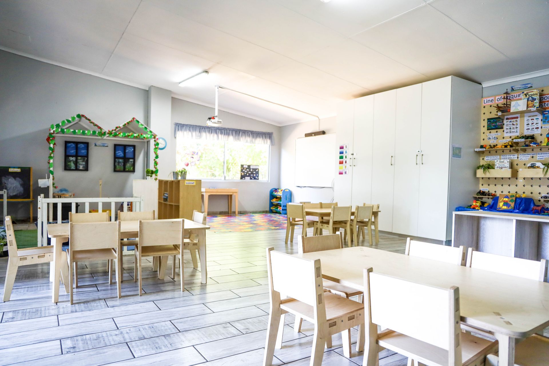 A classroom with tables and chairs and a playhouse.