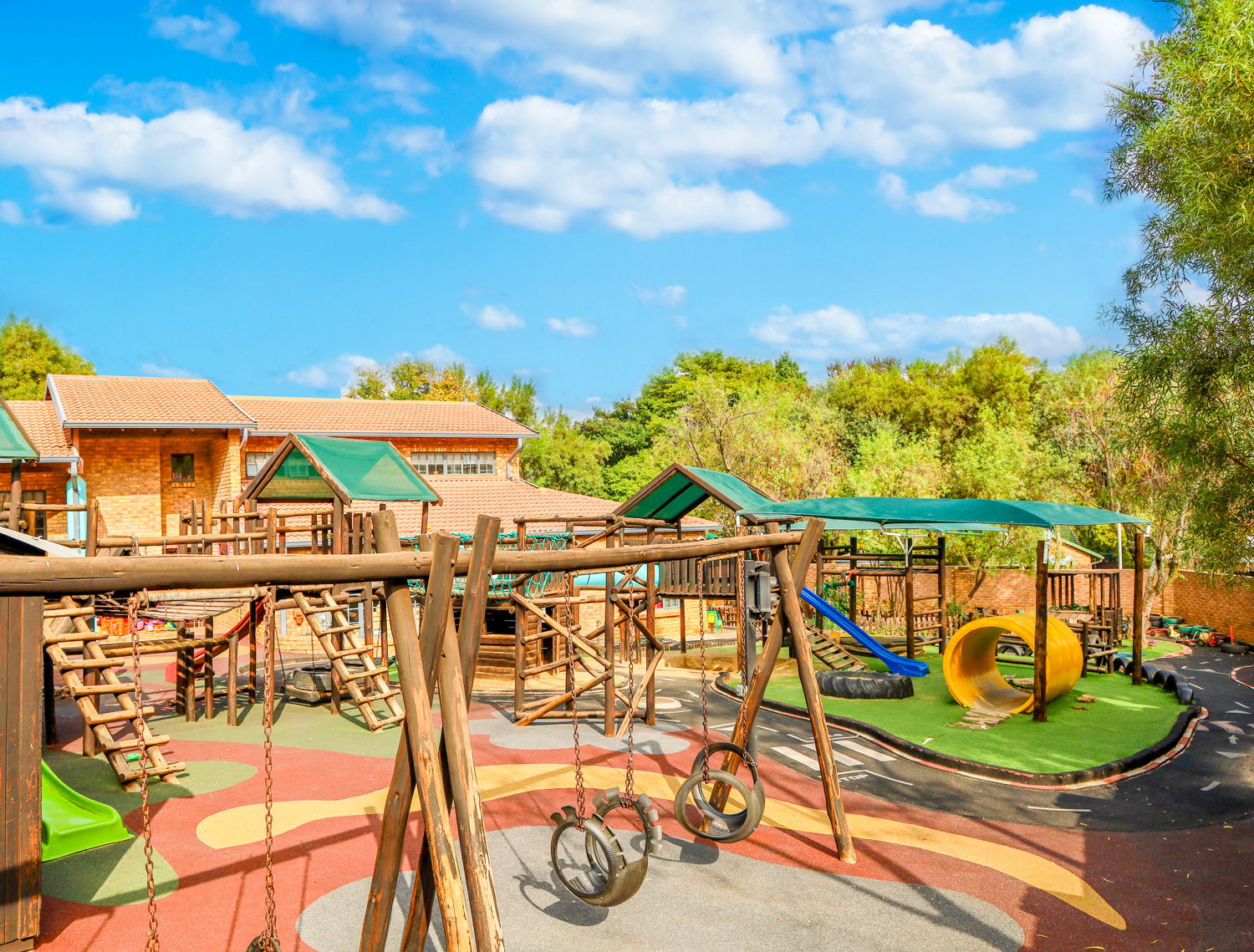 A playground with swings , a slide , and a house in the background.
