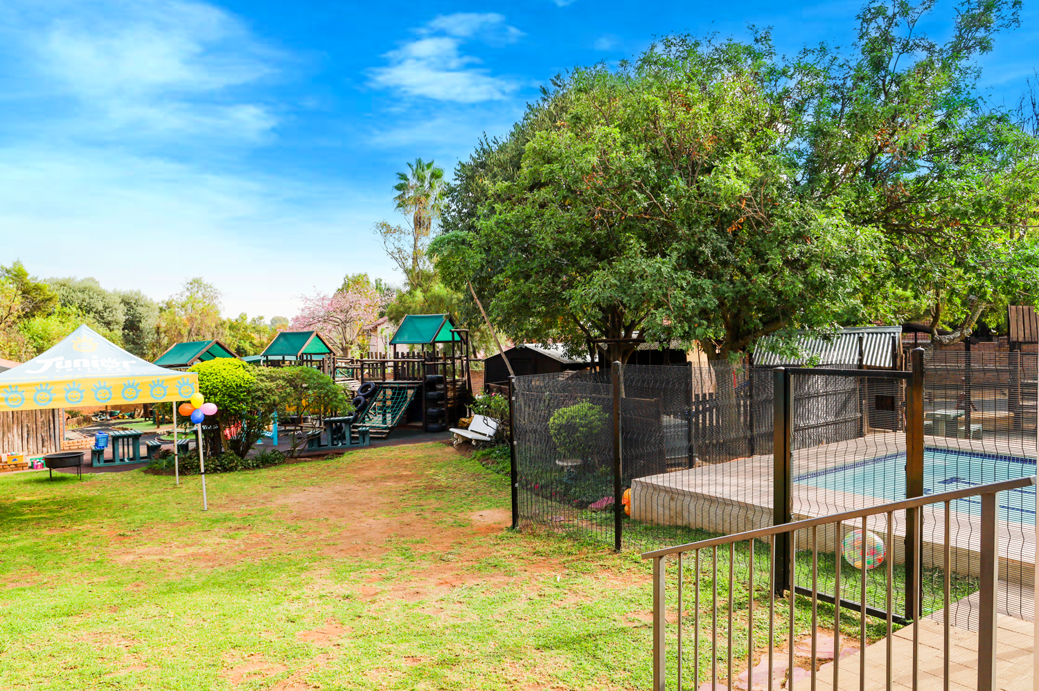 A fenced in yard with a swimming pool and a playground in the background.