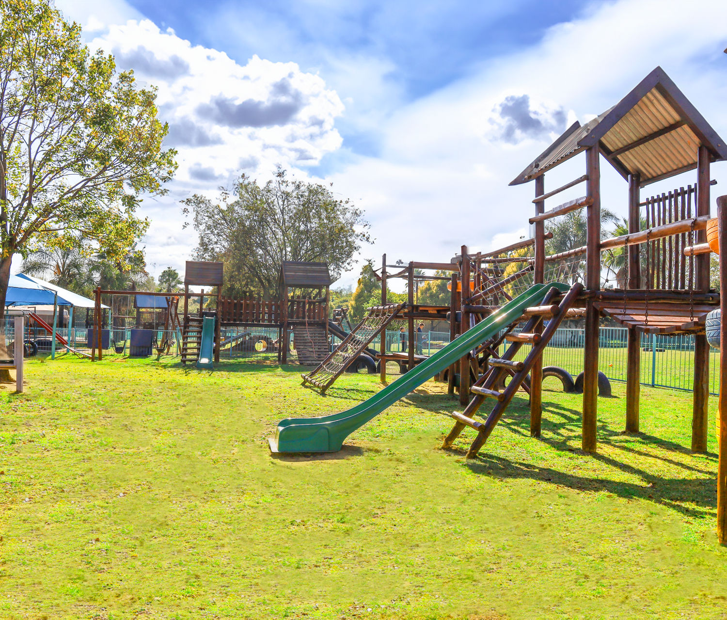 A playground with a slide , stairs , and swings in a grassy field.