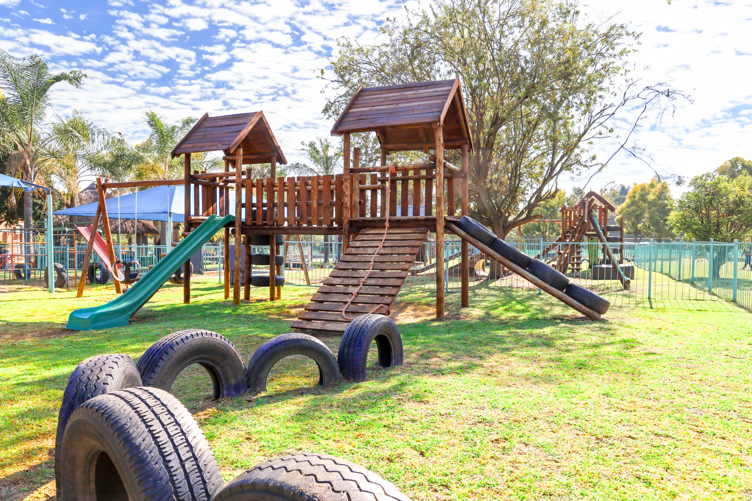 A playground with tires in the foreground and a slide in the background.