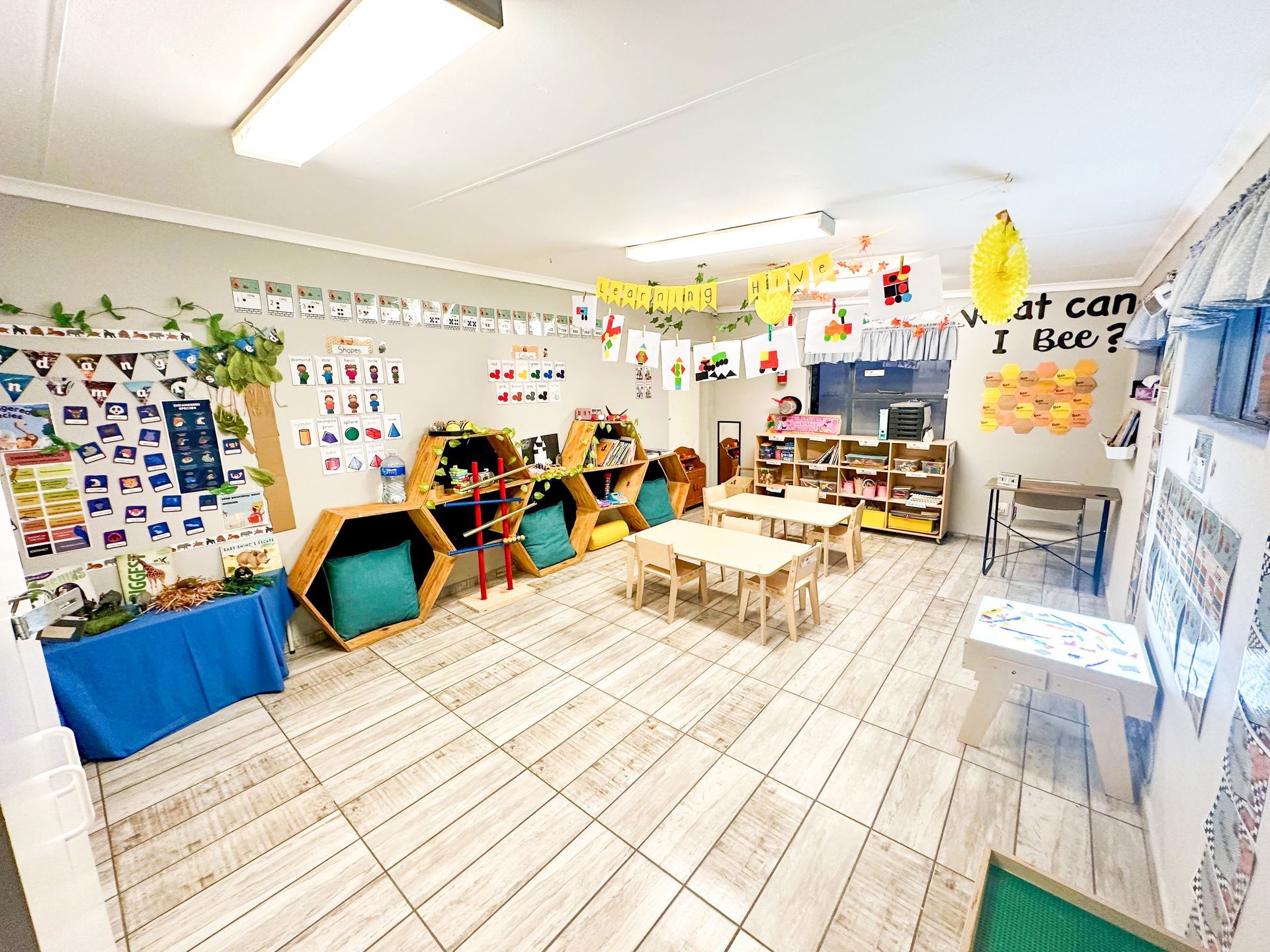 A classroom with tables , chairs , and shelves.