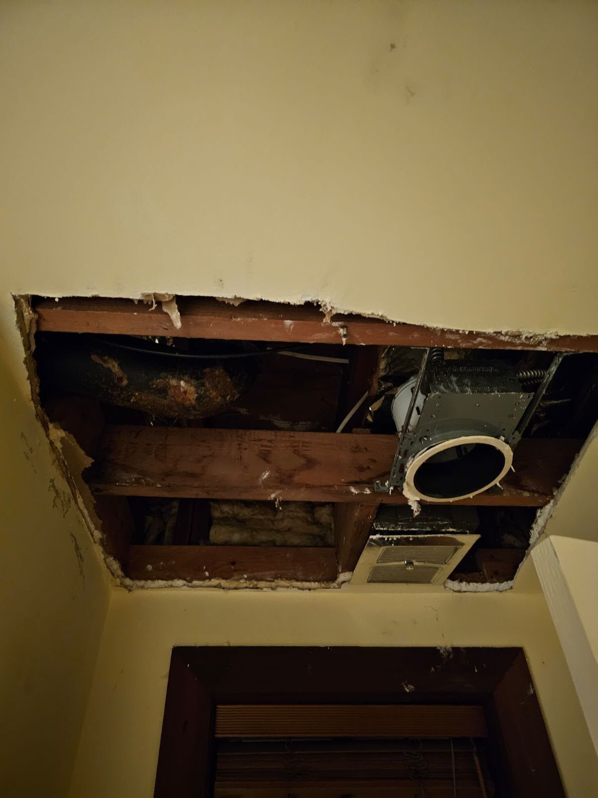 A hole in the ceiling of a room with a fan coming out of it.