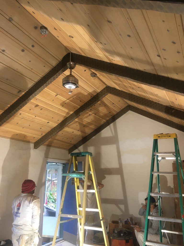 A man is standing next to a ladder in a room with a wooden ceiling.