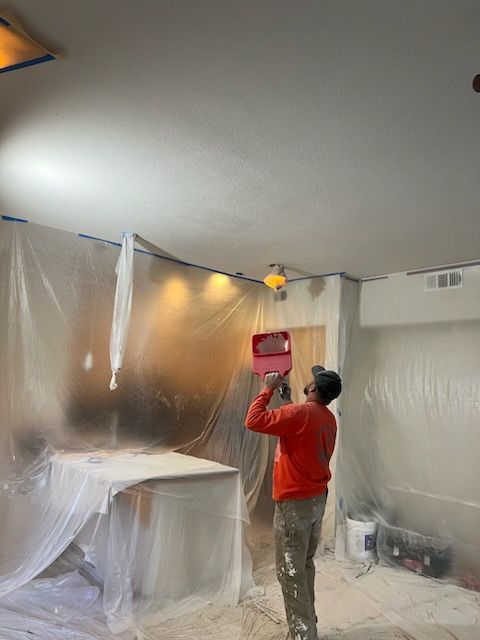 A man is painting the ceiling of a room with a sprayer.