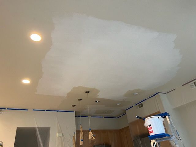 A ceiling is being painted in a kitchen with a ladder.
