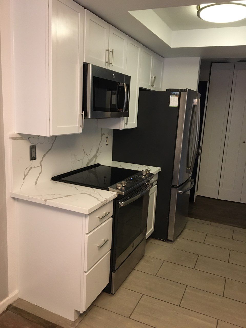 A kitchen with white cabinets , a stove , a refrigerator , and a microwave.