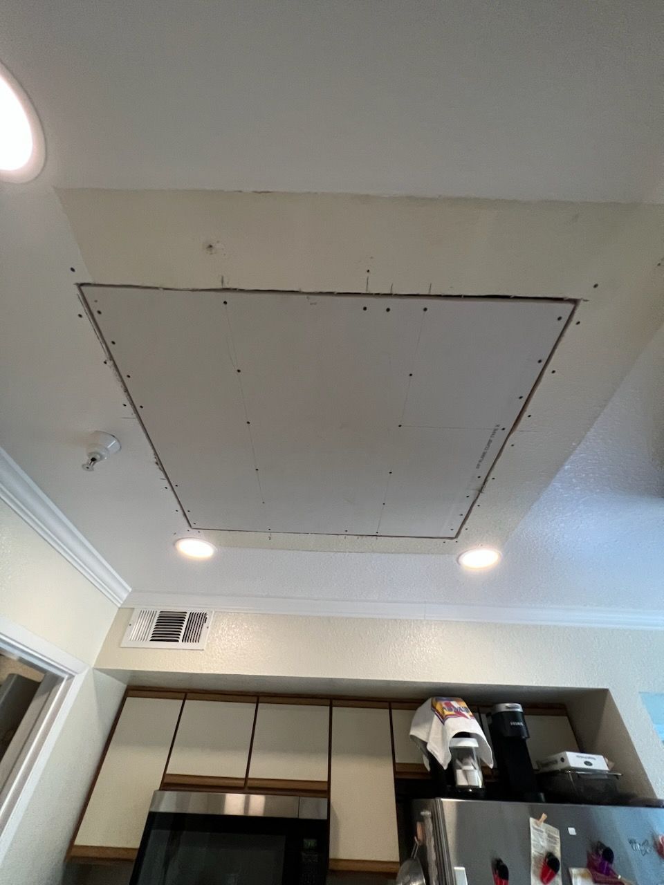 A kitchen with a ceiling that has a square hole in it.