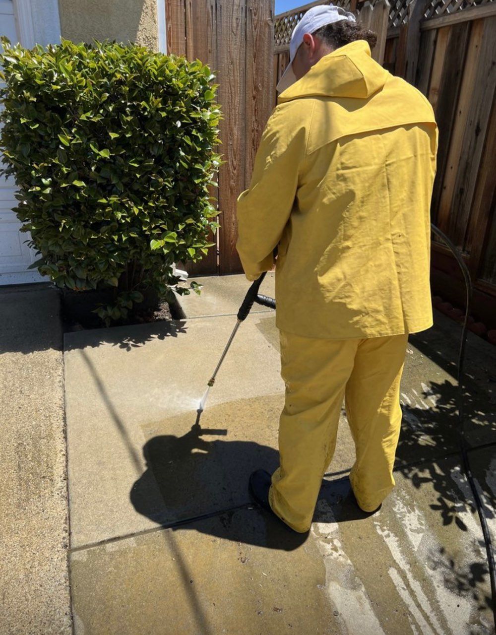 A man in a yellow raincoat is cleaning a sidewalk with a pressure washer