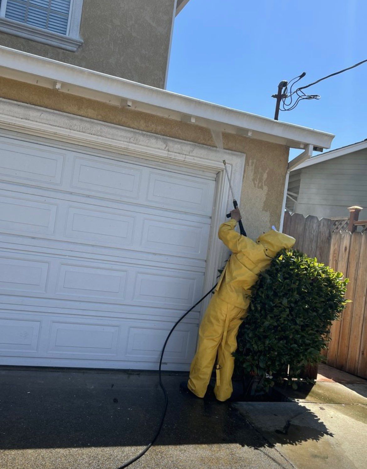 A person in a yellow suit is cleaning a garage door with a high pressure washer.
