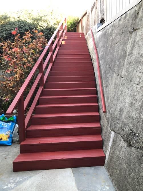 A set of red stairs with a red railing leading up to a house.