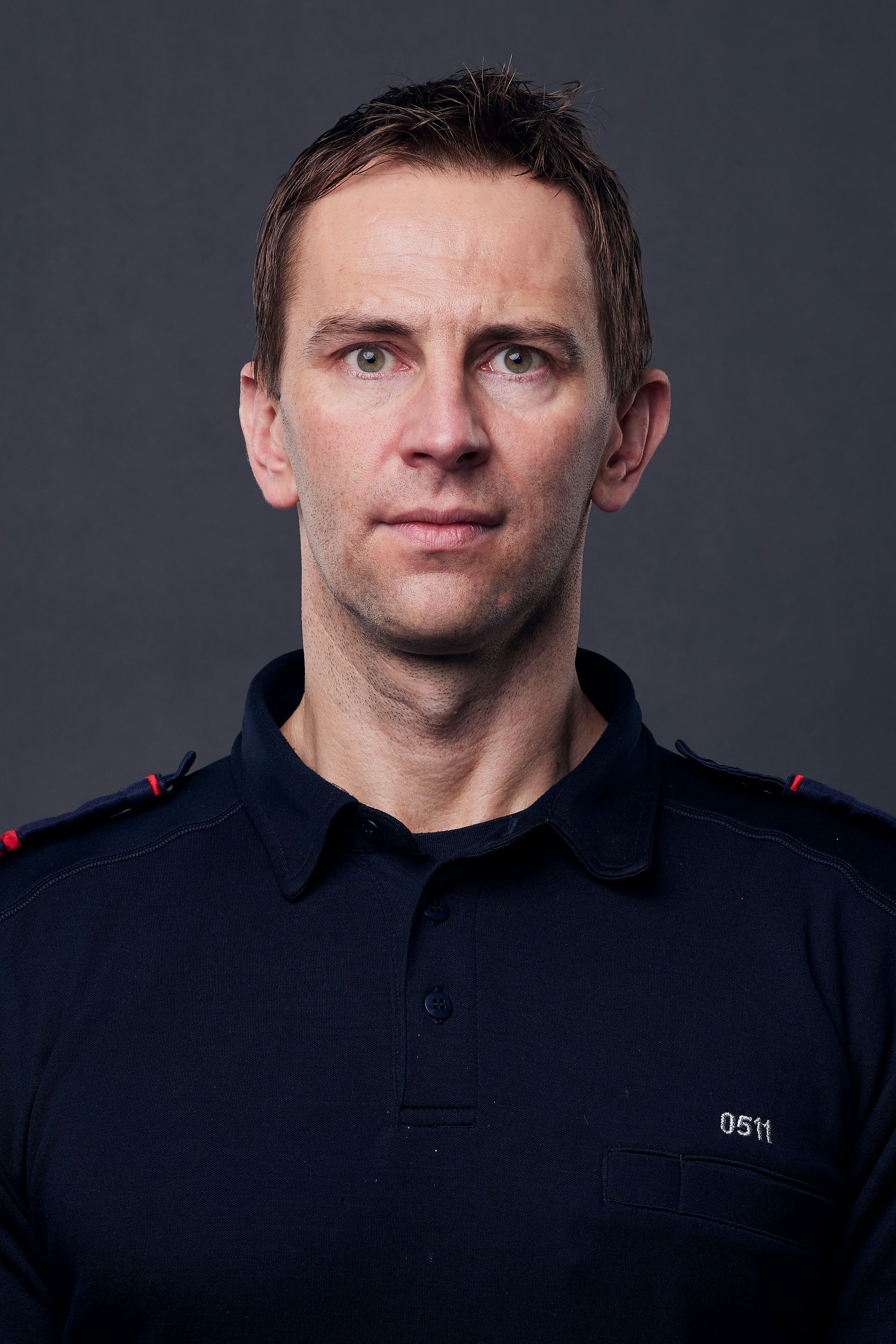 Man with short brown hair in a navy blue shirt against a gray background.
