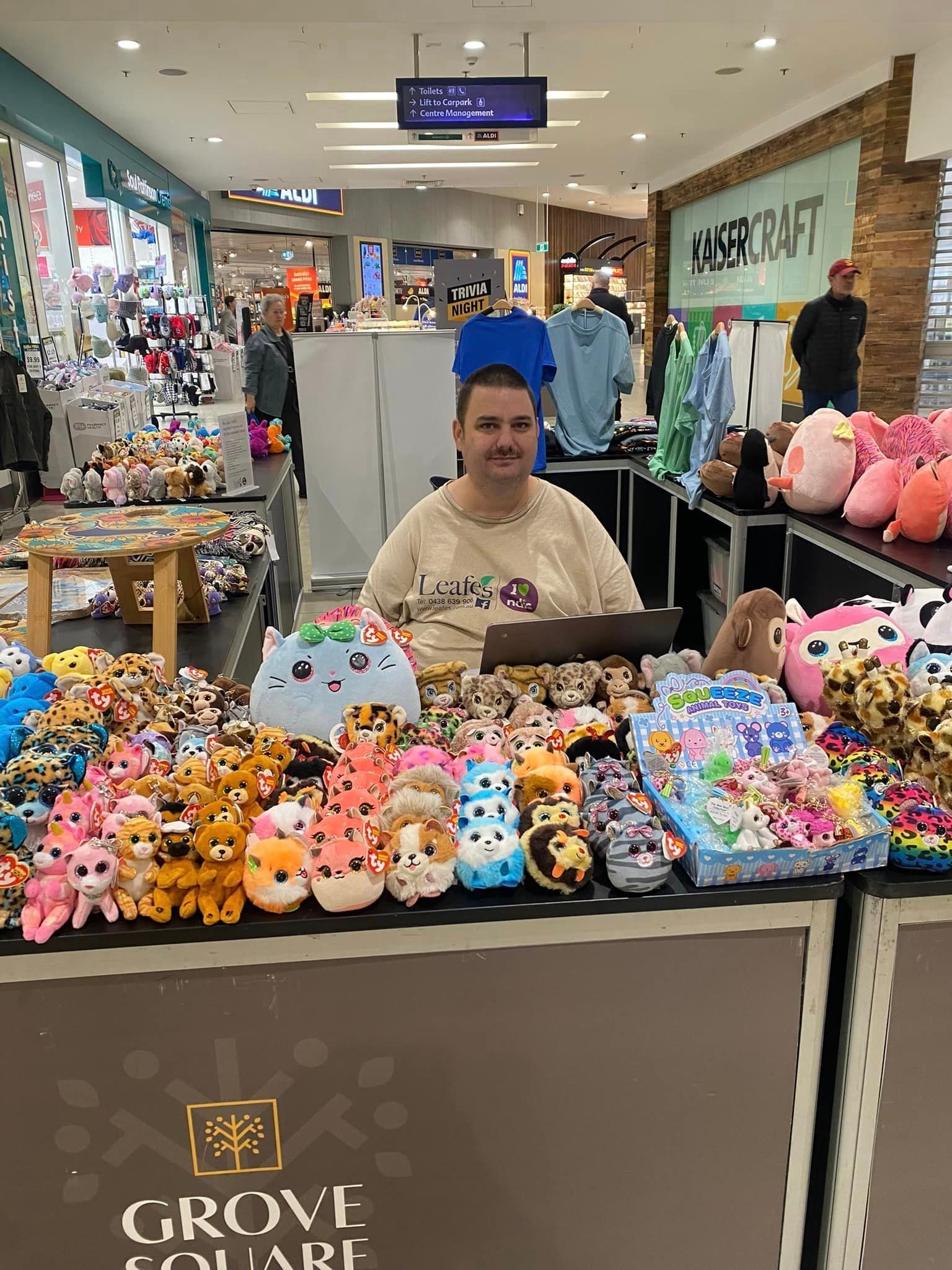 A man is sitting in front of a table full of stuffed animals.